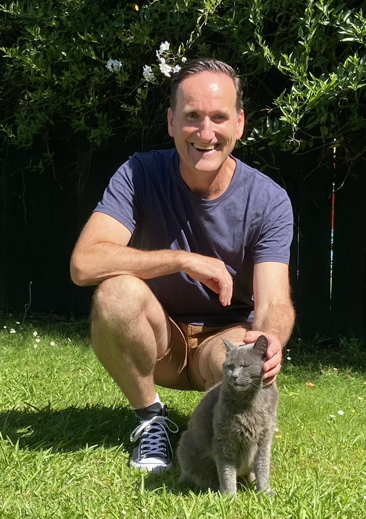 Steve Mullan smiling with a grey cat in a sunny garden