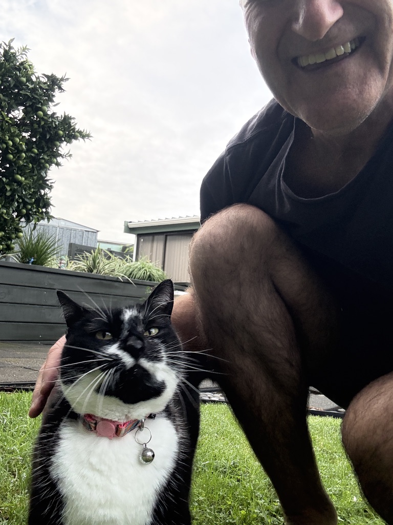 Steve Mullan smiling with a black and white cat on a lawn